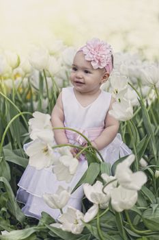 Little girl in an elegant dress to stand near blossoming tulips