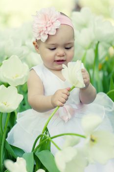 Little girl in an elegant dress to stand near blossoming tulips