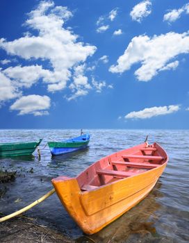 Three colored wooden boats on a leash in water near bank