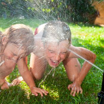 Little girl and boy palying with lawn sprinkler