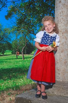 Small Bavarian girl in a dirndl with sunflower in her hand