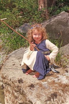 Little girl in medieval dress sitting on a rock while fishing