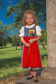 Blond girl in dirndl with blond hair posing with a sunflower in the hands