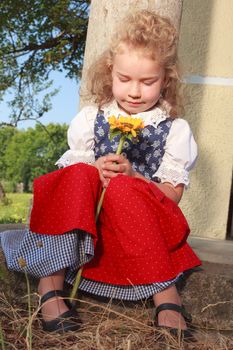 Young little girl looking at the flower while leaning on the wall
