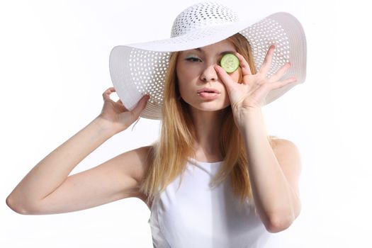 Portrait of young adult Caucasian woman on white background holding cucumber slices over her eyes.
