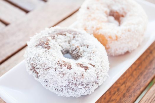 Chocolate and vanilla coconut donuts on wooden table, stock photo