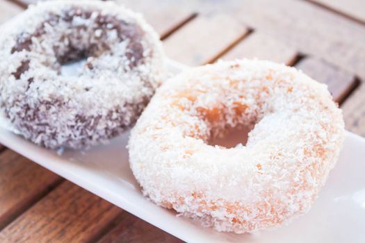 Vanilla and chocolate coconut donuts on wooden table, stock photo