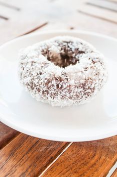 Piece of chocolate coconut donut on white plate, stock photo