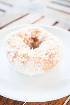 Piece of vanilla coconut donut on white plate, stock photo