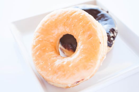 Glazed and chocolate donuts on white plate, stock photo