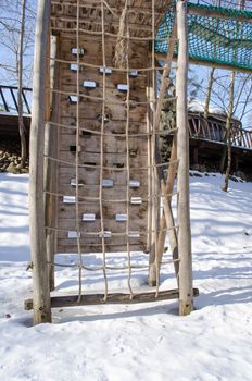 rope for climbing on wooden construction surrounded by snow in winter playground.