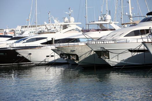 Row of luxury motorised yachts moored in a sheltered harbour, close up view of the bows