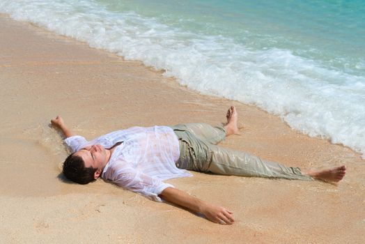 Tired out man lie on sandy beach near the blue sea