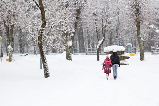 snowfall in city park, two people walking