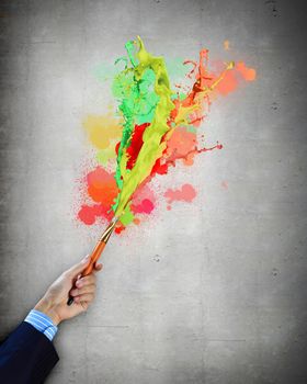 Close-up of human hand holding paint brush making colorful paint splashes