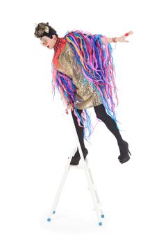 Fashion conscious drag queen in a glitzy gold dress, high heeled stilettos and with streamers performing in a show, isolated on white