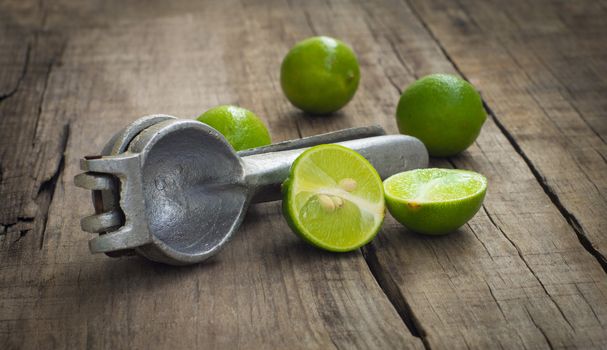 Old hand juicer with limes on wooden background