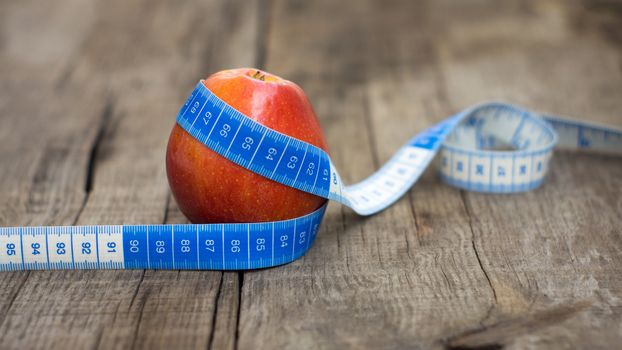 Measuring tape wrapped around a red apple on wooden background.