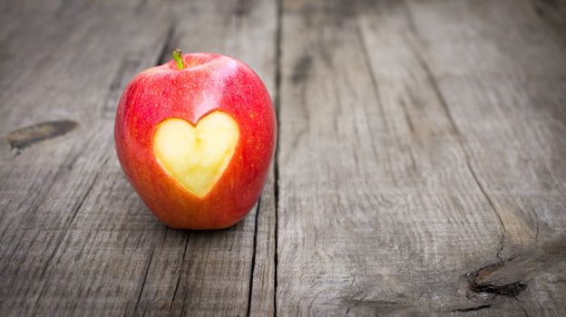 Apple with engraved heart on wood background