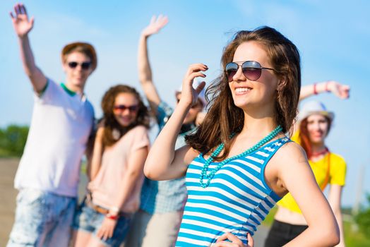 stylish young woman in sunglasses on the background of blue sky and friends