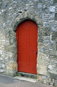 Old wooden red door surrounded by weathered stone in Arundel a historic town in England.