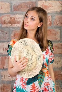 Portrait of pensive girl with a straw hat in hand against a vintage brick wall.