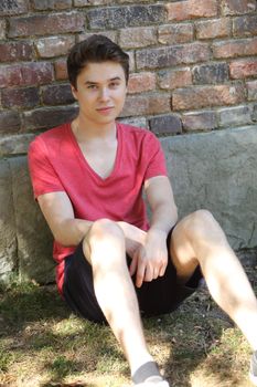 Handsome teenage boy sitting on the ground leaning against a wall relaxing in the shade