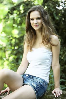 Beautiful young woman sitting in the shade of a tree in the garden in her summer shorts enjoying her vacation from college