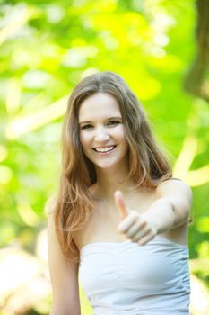 Happy young woman giving a thumbs up gesture of approval and success while standing outdoors in a lush garden