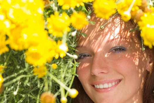 Beautiful girl laying on a field among fresh grass & yellow flowers.