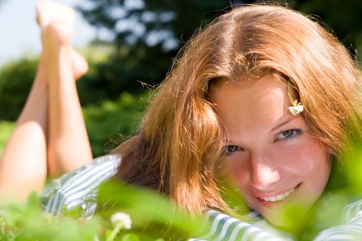 Beautiful girl laying on a field among fresh grass & yellow flowers.