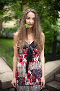 Beautiful girl with a maple leaf in her mouth. Green leaves  background.