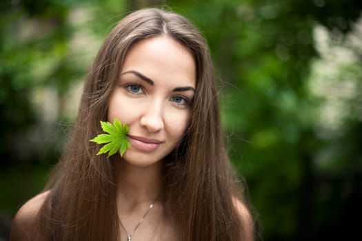 Beautiful girl with a maple leaf in her mouth. Green leaves  background. Nature.