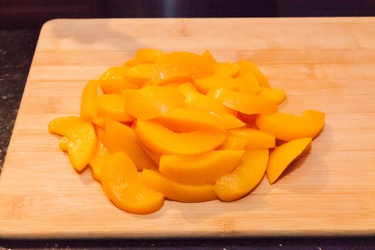 Sliced apricots on wooded cutting board prepared for layer cake.