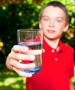 Boy holding glass of water outdoors, focus on glass