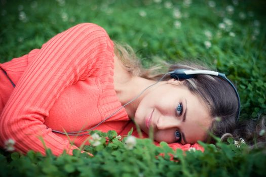 Relaxed young woman listening musi cat clover meadow