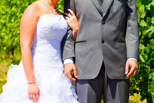 A bride and groom are close together showing just their torso arms and hands while holding each other after their wedding.