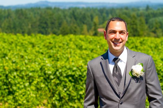 An attractive groom poses for a portrait on his happy wedding day outside at a winery vineyard in Oregon during the summer.