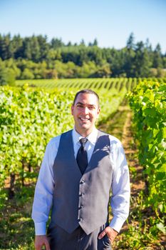 An attractive groom poses for a portrait on his happy wedding day outside at a winery vineyard in Oregon during the summer.