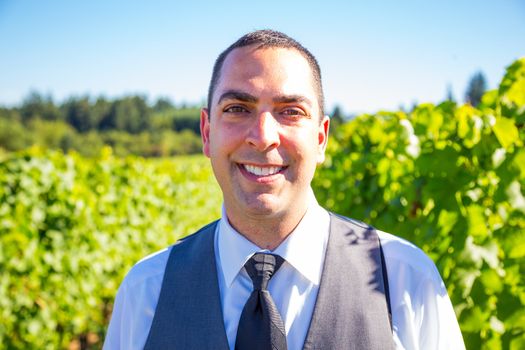 An attractive groom poses for a portrait on his happy wedding day outside at a winery vineyard in Oregon during the summer.