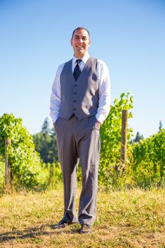 An attractive groom poses for a portrait on his happy wedding day outside at a winery vineyard in Oregon during the summer.