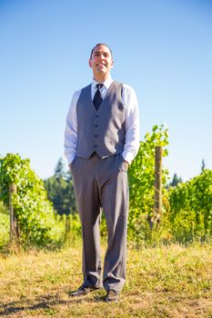 An attractive groom poses for a portrait on his happy wedding day outside at a winery vineyard in Oregon during the summer.