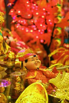 Smiling Chinese ceramic mandarin doll amongst gold trinkets representing wealth and prosperity. A colourful decoraton for the Chinese New Year in Kuala Lumpur