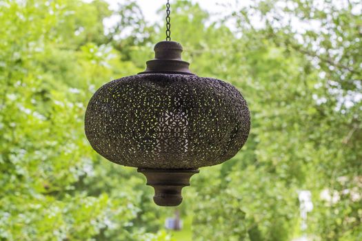 A vintage porch light hanging with a view of trees in the background.