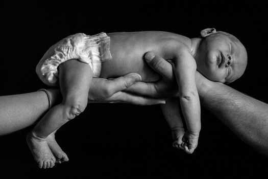 A black and white shot of a newborn baby boy being held up by two hands.