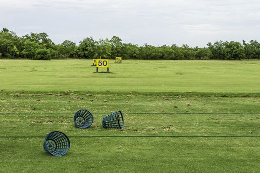 A driving range shot showing yardage signs and empty golf ball baskets.