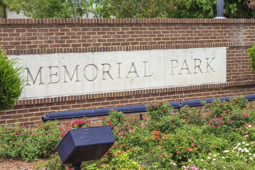 An entrance sign for a memorial park with red brick and surrounded by plants.