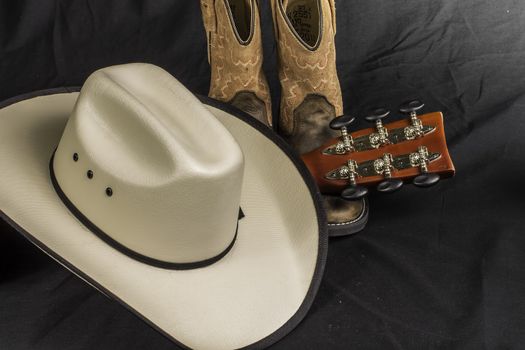 A close shot of a pair of boots. cowboy hat and a guitar handle.