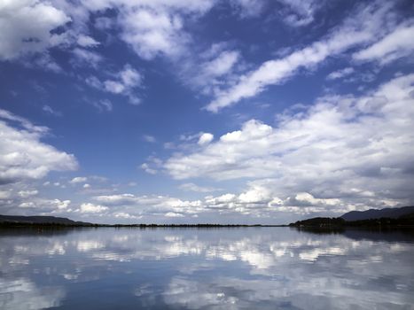 Reflection of white clouds on blue sky background in the lake Kochel in Bavaria, Germany