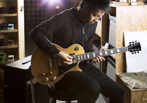 A young asian teenager playing electric guitar with a spotlight shining from the back.